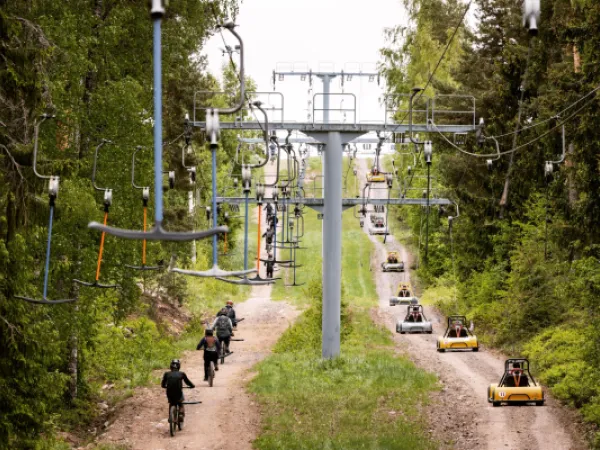 Alamäkipyöräilijöitä ja mäkiautoja ankkurihississä menossa mäkeä ylös.