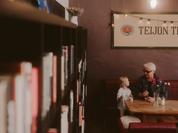 Lapsi ja isoäiti istumassa kahvilan sohvalla ja syömässä jäätelöä.